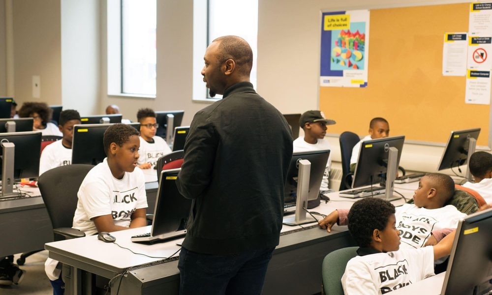 A volunteer communicating with students at a Black Boys Code Workshop
